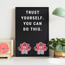 Motivational quote on a black letter board with cartoon characters, placed on a white surface with decor elements.