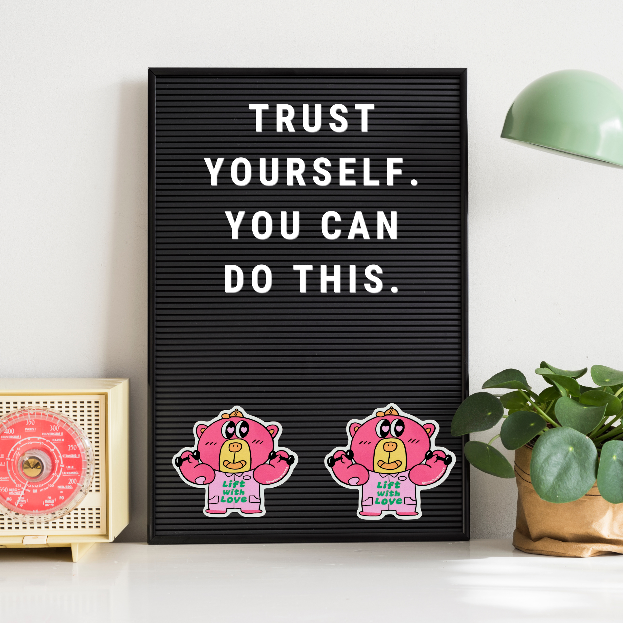 Motivational quote on a black letter board with cartoon characters, placed on a white surface with decor elements.