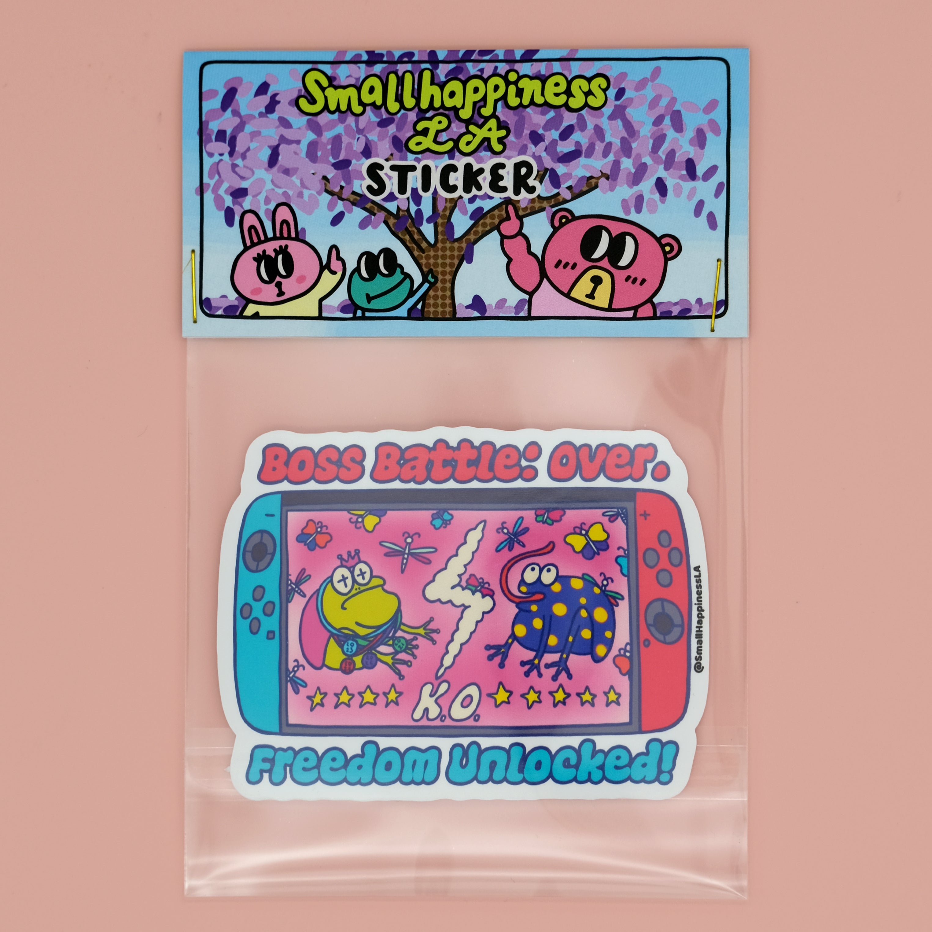 Boss Battle Frog vinyl sticker featuring two cartoon frogs battling on a handheld gaming console screen with the words “Boss Battle: Over” and “Freedom Unlocked” in bold, colorful text, packaged in clear plastic bag branded by SmallHappinessLA