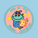 Circular patch with cartoon frog character holding a sticker book and text 'Lost in my sticker universe' on a pink background designed by SmallHappinessLA