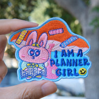 Colorful planner girl embroidery patch held by a hand with a blurred natural background.

