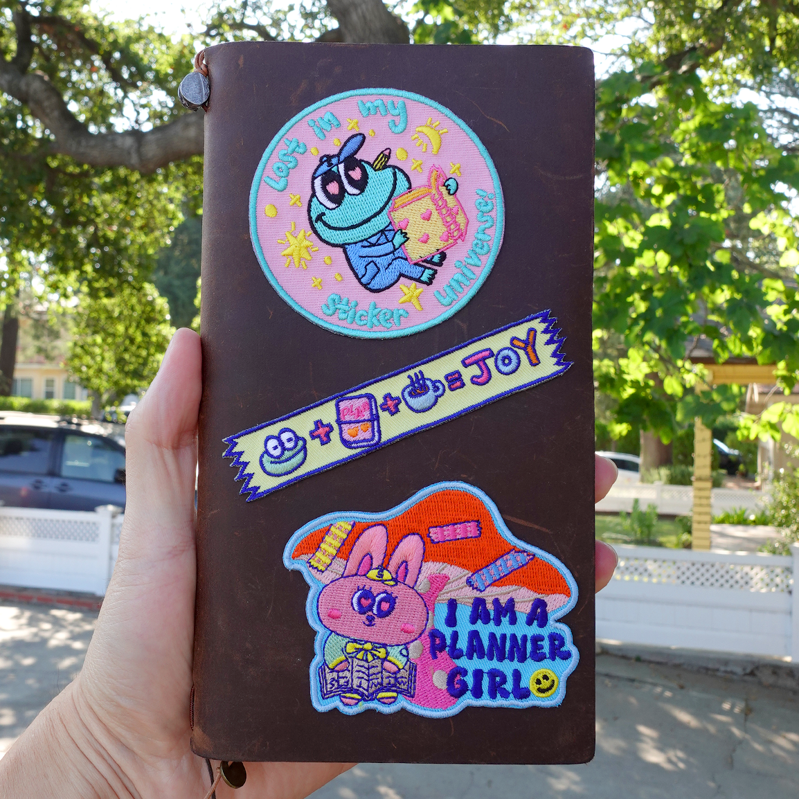 Brown notebook with colorful stickers held outdoors