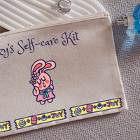 Self-care kit pouch with cartoon characters and text on a textured surface