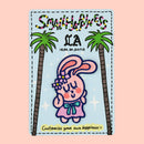 Self-love bunny iron-on embroidery patch on graffiti backing card, displayed against a rose pink background.