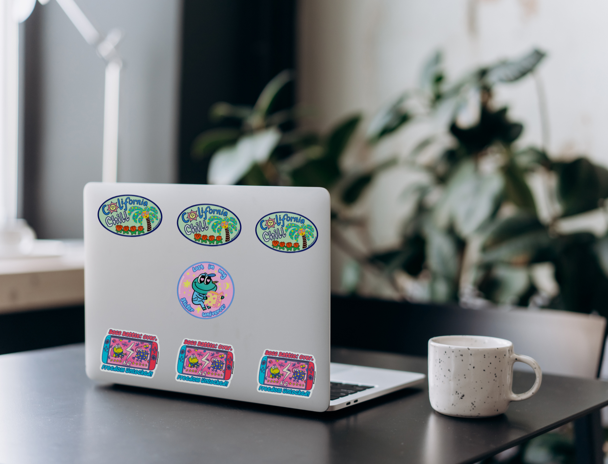 Laptop with colorful stickers on a desk next to a mug, with a blurred plant in the background 