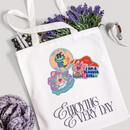 Tote bag with cartoon designs and text, surrounded by lavender and pens on a light background