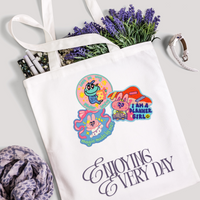 Tote bag with cartoon designs and text, surrounded by lavender and pens on a light background