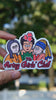 Artsy Girls Club vinyl sticker featuring cartoon versions of iconic women artists, including Mona Lisa, Frida Kahlo, and Girl with a Pearl Earring, on a pink background held by hand in natural day light
